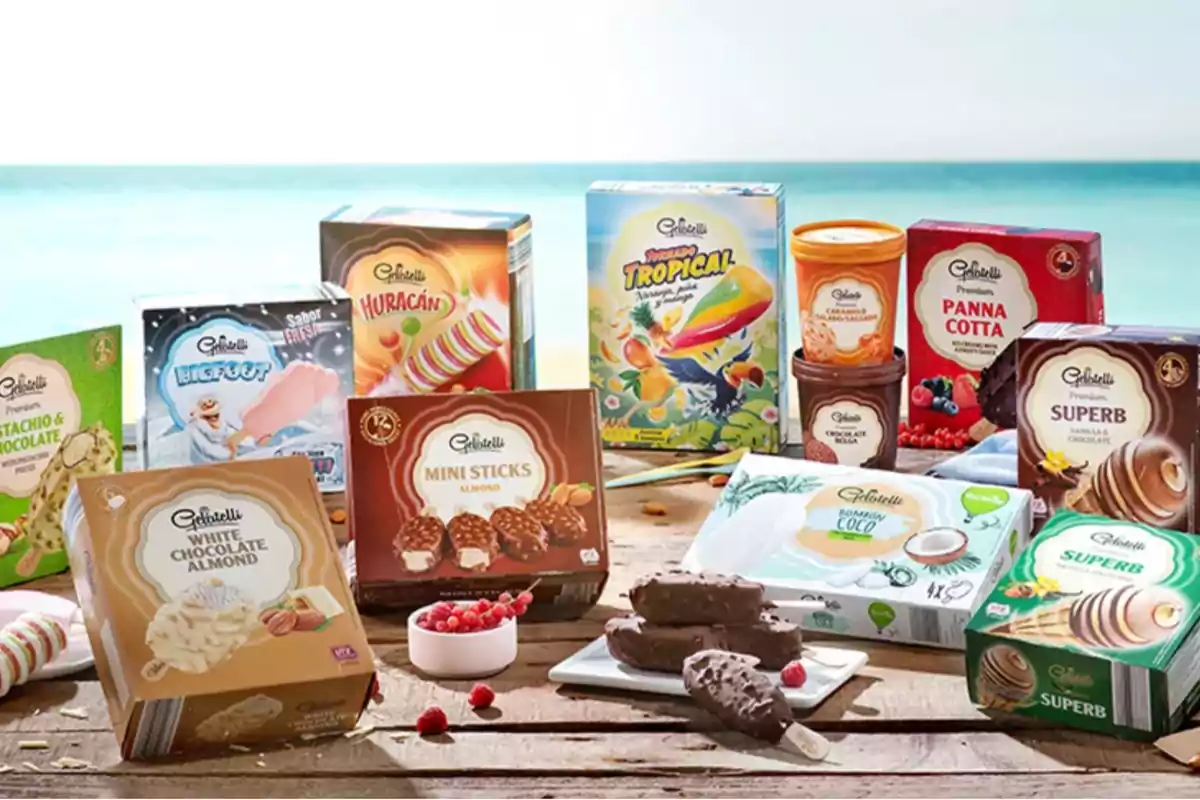 Una varietat de gelats i postres congelades de la marca Gelatelli s'exhibeixen sobre una taula de fusta amb un fons de platja i mar.