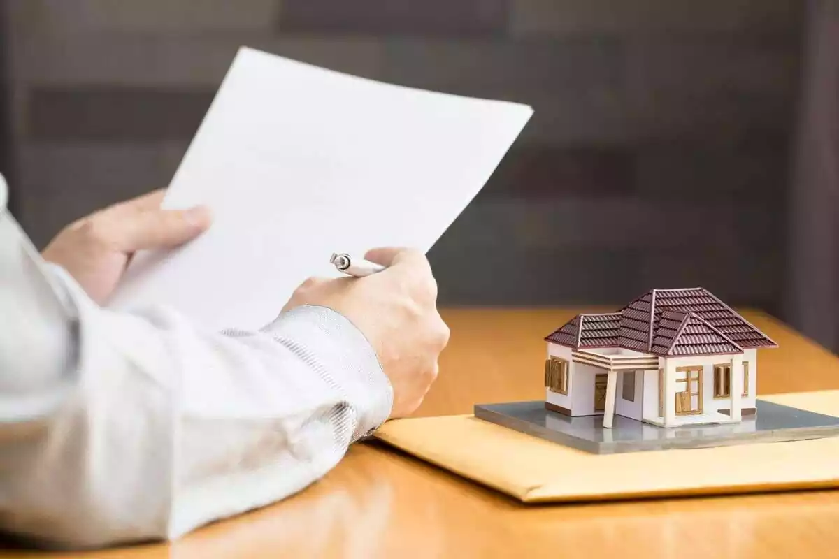 Una persona amb un paper i un boli i una maqueta duna casa en miniatura sobre una taula