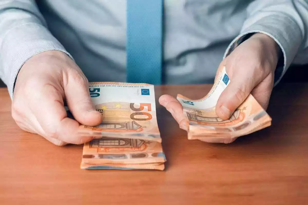 Mans d'un home amb camisa i corbata blava, comptant bitllets de 50 euros
