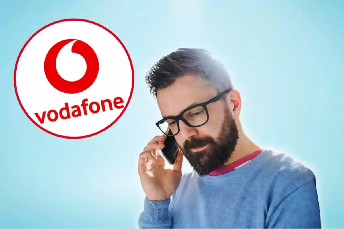 Home amb barba i ulleres parlant per telèfon mòbil amb el logotip de Vodafone al fons.