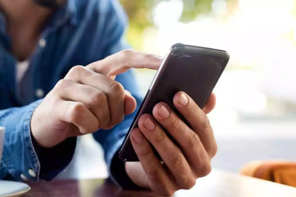 Mans d'un home amb camisa texana fent servir un telèfon tàctil