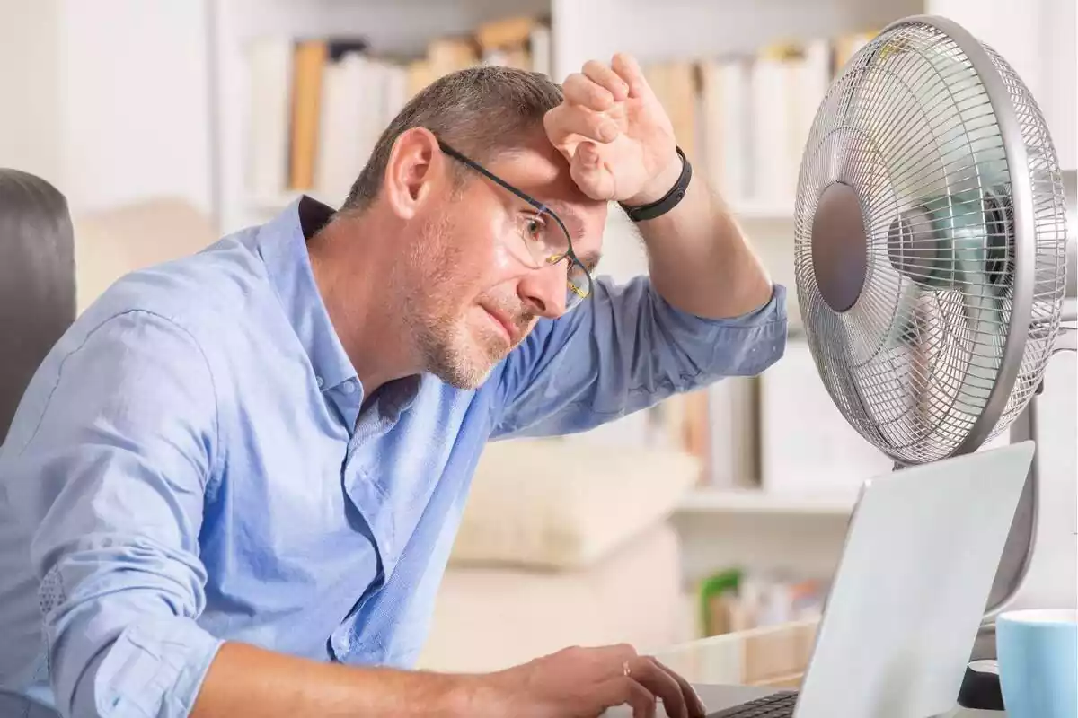 Un home utilitzant un ordinador portàtil davant d'un ventilador encès