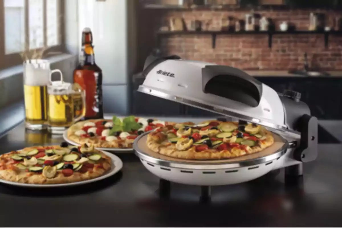 Una màquina per fer pizzes amb una pizza acabada de fer i una altra pizza en un plat al costat, acompanyades d'una gerra de cervesa i una ampolla en una cuina moderna. Una màquina per fer pizzes amb una pizza acabada de fer i una altra pizza en un plat al costat, acompanyades d'una gerra de cervesa i una ampolla en una cuina moderna.
