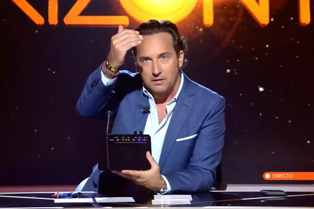 Iker Jiménez en un plató de televisió, vestit amb un vestit blau, sosté un dispositiu negre mentre gesticula amb la mà. Captura de 'Horizonte' Iker Jiménez en un plató de televisió, vestit amb un vestit blau, sosté un dispositiu negre mentre gesticula amb la mà. Captura de 'Horizonte'