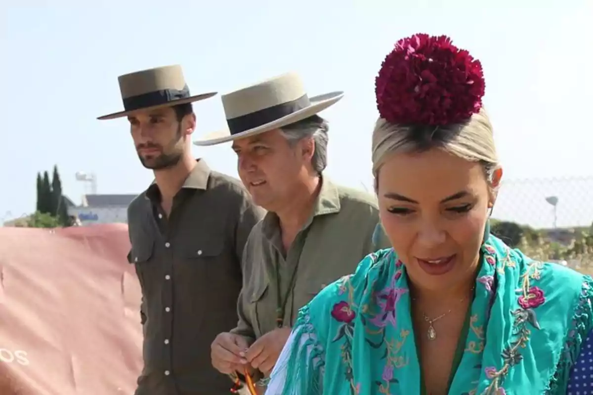 Tres persones vestides amb vestits típics andalusos, dos homes amb barret d’ala ampla i una dona amb mantó turquesa brodat i una flor vermella als cabells, en un ambient a l’aire lliure i assolellat. Tres persones vestides amb vestits típics andalusos, dos homes amb barret d’ala ampla i una dona amb mantó turquesa brodat i una flor vermella als cabells, en un ambient a l’aire lliure i assolellat.