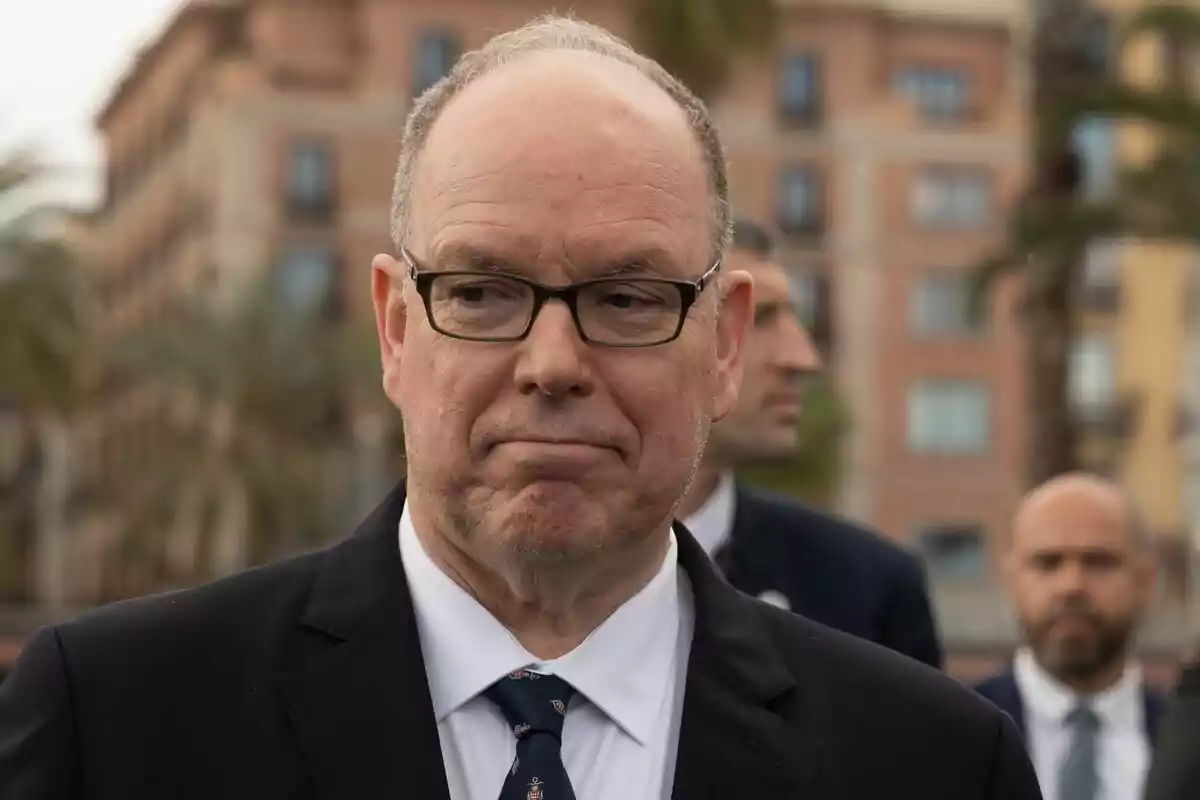A man with glasses and a dark suit in an urban setting. A man with glasses and a dark suit in an urban setting.