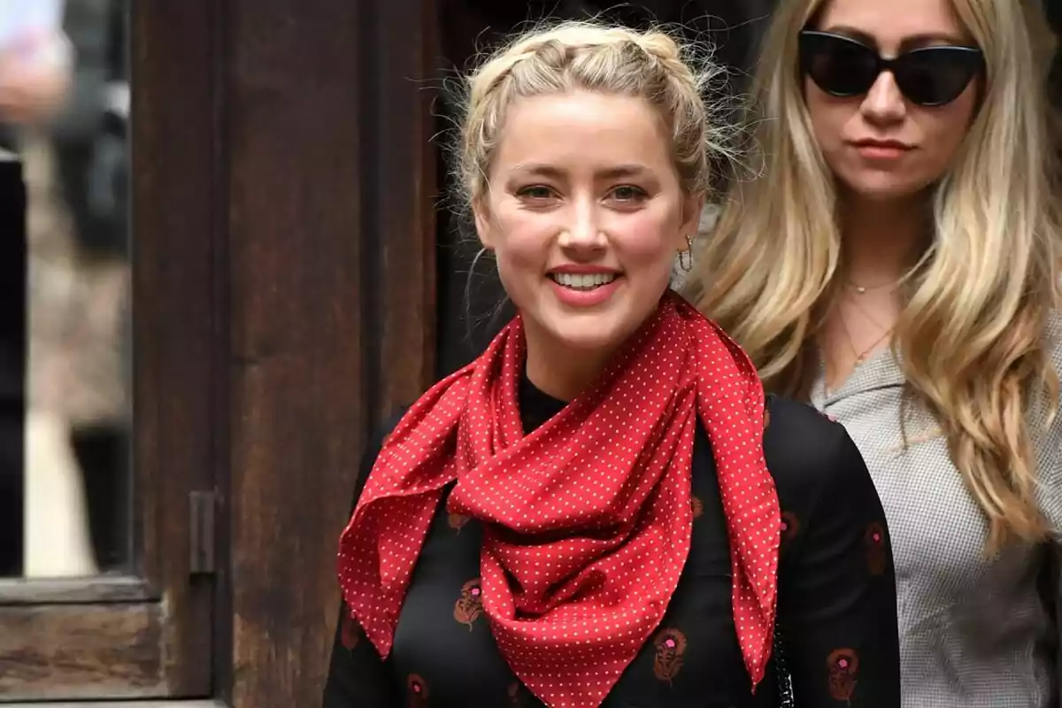 A person with a red scarf with white polka dots and a braid in their hair smiles while standing next to another person with sunglasses. A person with a red scarf with white polka dots and a braid in their hair smiles while standing next to another person with sunglasses.