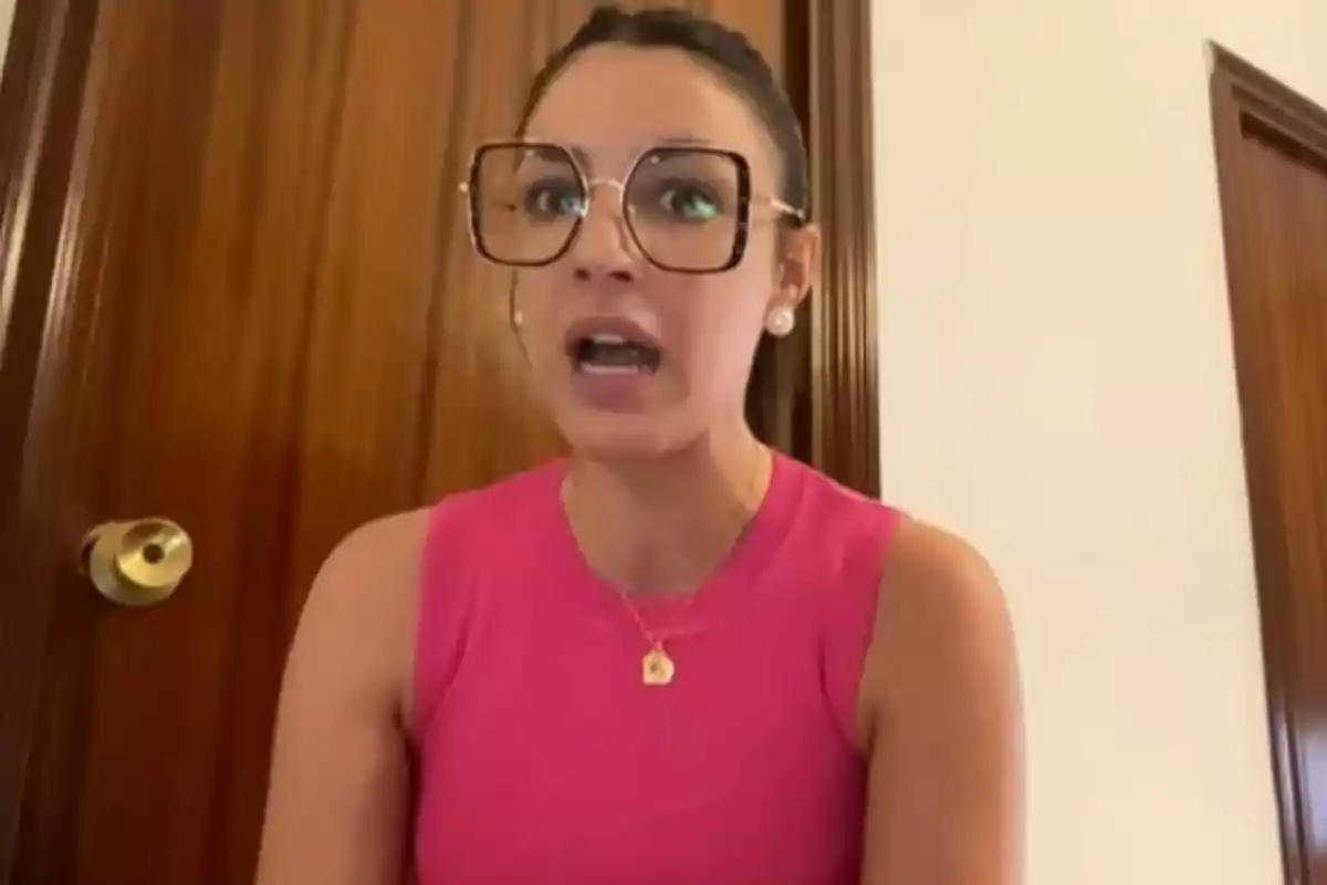 Dona amb ulleres grans i brusa rosa parlant davant d'una porta de fusta. Dona amb ulleres grans i brusa rosa parlant davant d'una porta de fusta.