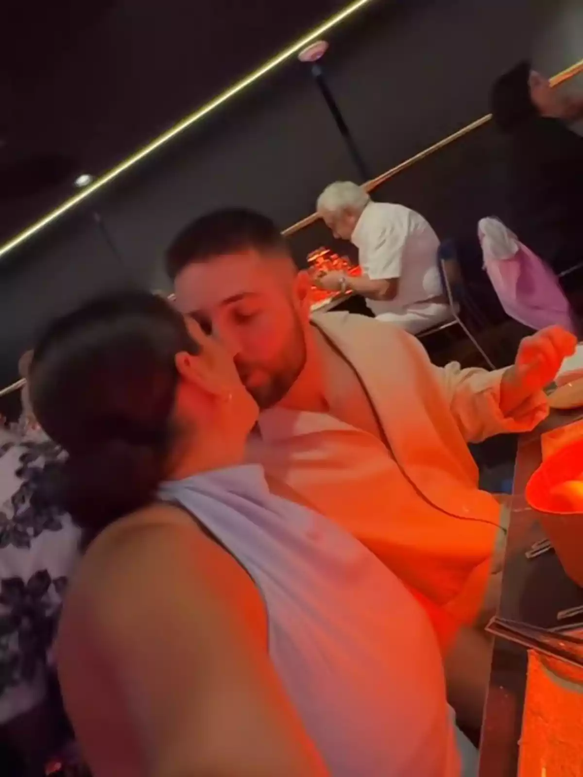 Parella besant-se en un restaurant amb llum tènue i ambient íntim Parella besant-se en un restaurant amb llum tènue i ambient íntim