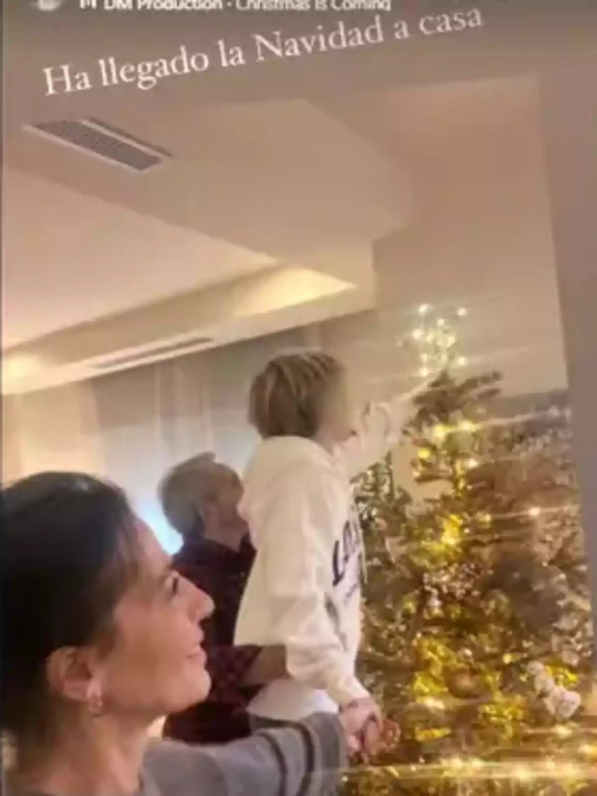 Ángeles Blanco, Vicente Vallés i el seu fill decorant un arbre de Nadal amb llums brillants a una sala il·luminada.