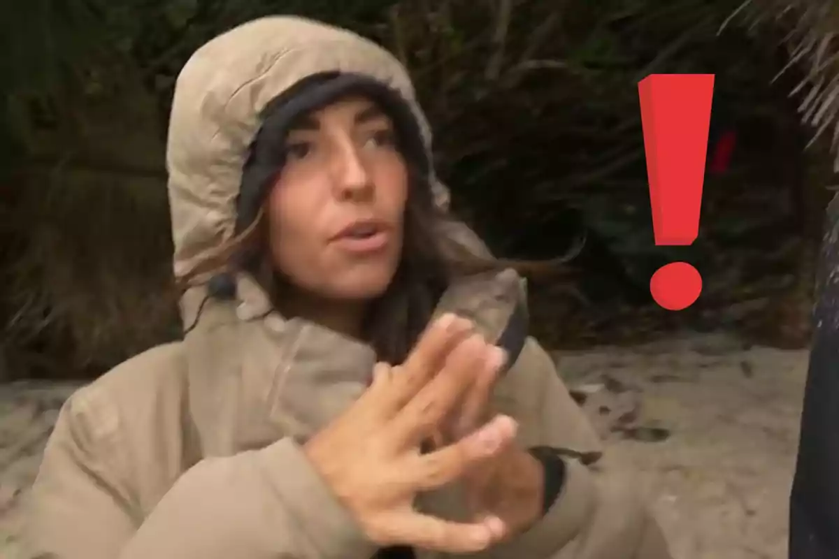 Una persona amb jaqueta gruixuda i caputxa està gesticulant amb les mans en un entorn a l'aire lliure amb un signe d'exclamació vermell al costat.
