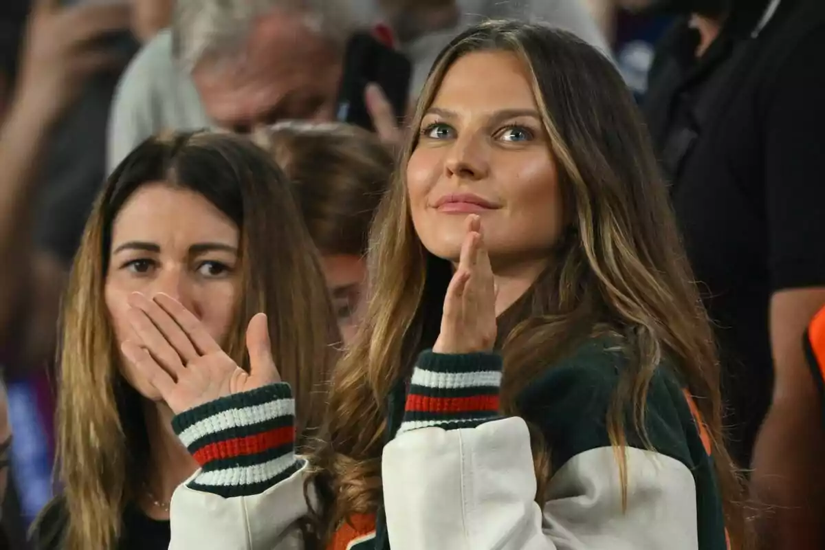 Dos mujeres en un evento deportivo, una de ellas aplaudiendo y la otra con la mano cerca de la boca, rodeadas de más personas en el fondo. Dos mujeres en un evento deportivo, una de ellas aplaudiendo y la otra con la mano cerca de la boca, rodeadas de más personas en el fondo.