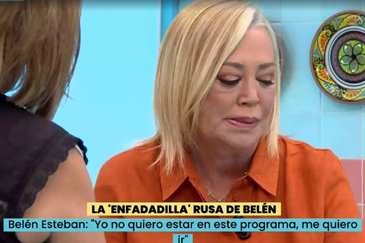 Una dona amb cabell ros i camisa taronja sembla estar en un programa de televisió, amb un text a la part inferior que indica el seu desig de marxar. Una dona amb cabell ros i camisa taronja sembla estar en un programa de televisió, amb un text a la part inferior que indica el seu desig de marxar.