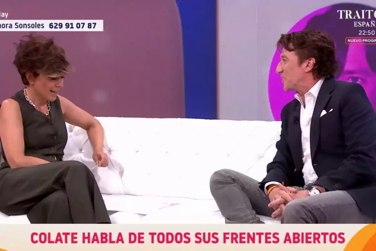 Dues persones conversen assegudes en un sofà blanc en un programa de televisió amb un fons morat i un text a la pantalla que diu Colate parla de tots els seus fronts oberts. Dues persones conversen assegudes en un sofà blanc en un programa de televisió amb un fons morat i un text a la pantalla que diu Colate parla de tots els seus fronts oberts.