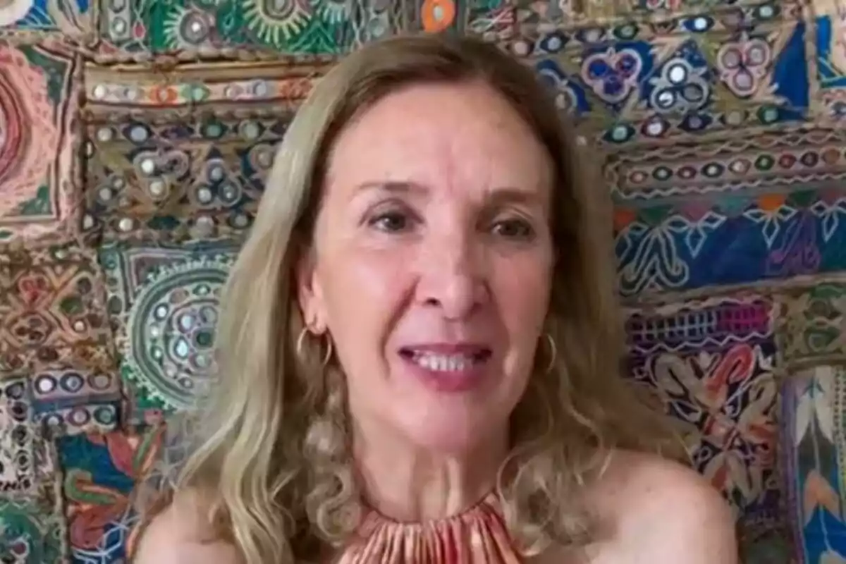 Una mujer de cabello rubio y rizado está frente a un fondo colorido con patrones geométricos y florales. Una mujer de cabello rubio y rizado está frente a un fondo colorido con patrones geométricos y florales.