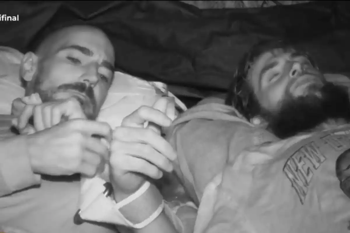 Dos homes estirats, un d’ells amb els ulls tancats i l’altre mirant cap endavant en una escena en blanc i negre. Dos homes estirats, un d’ells amb els ulls tancats i l’altre mirant cap endavant en una escena en blanc i negre.