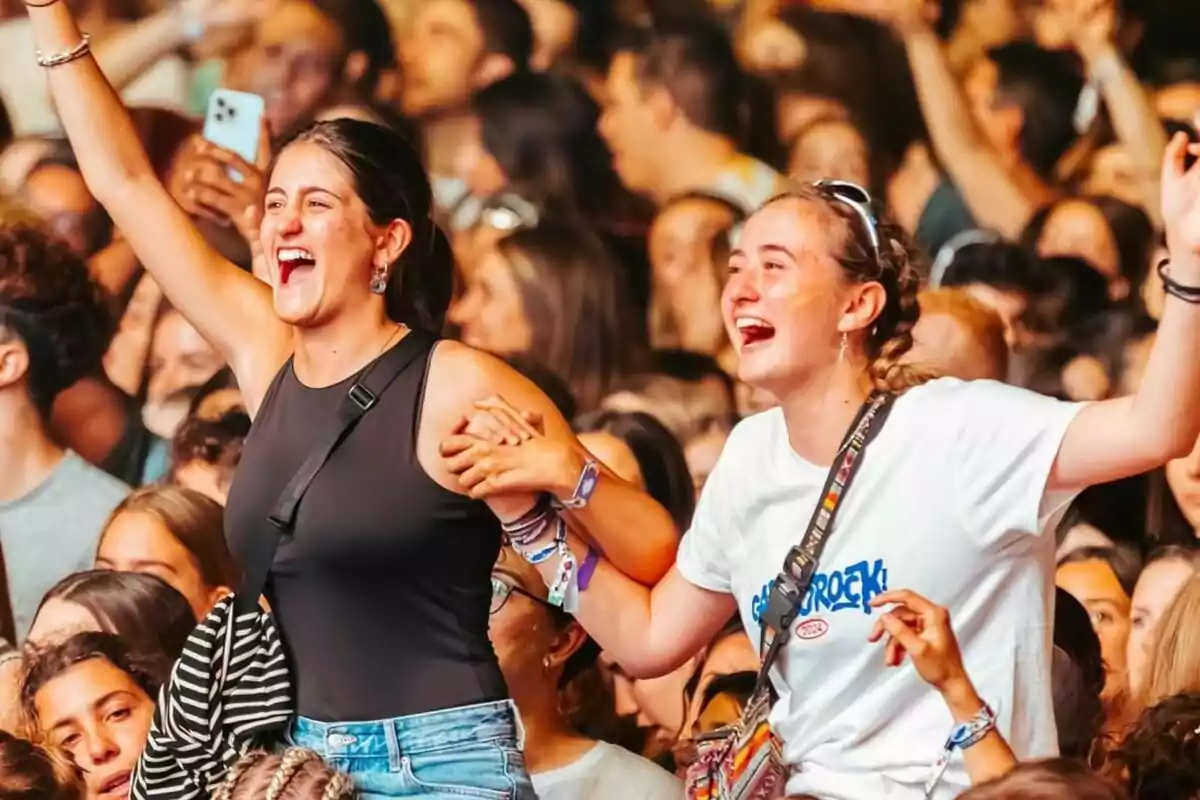 Dues noies somrients gaudeixen d’un concert entre una multitud, aixecant els braços i agafant-se de la mà mentre celebren emocionades. Dues noies somrients gaudeixen d’un concert entre una multitud, aixecant els braços i agafant-se de la mà mentre celebren emocionades.