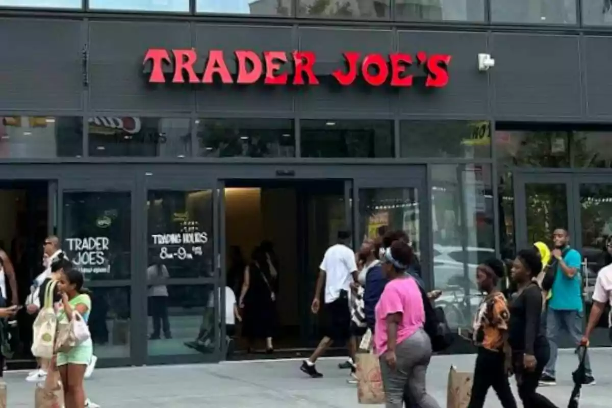 Facade of a Trader Joe's store with several people entering and exiting while carrying shopping bags. Facade of a Trader Joe's store with several people entering and exiting while carrying shopping bags.