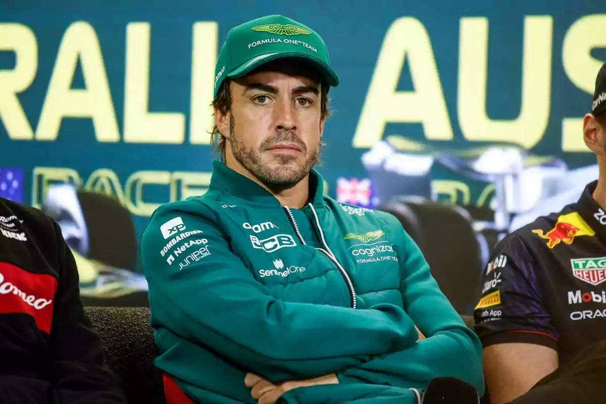 Motorsport driver wearing a green jacket and cap sitting with arms crossed during a Formula 1 press conference Motorsport driver wearing a green jacket and cap sitting with arms crossed during a Formula 1 press conference