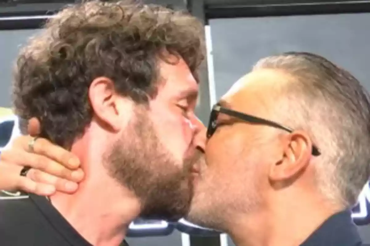 Dos homes es fan un petó als llavis mentre un d’ells sosté el clatell de l’altre amb la mà. Dos homes es fan un petó als llavis mentre un d’ells sosté el clatell de l’altre amb la mà.