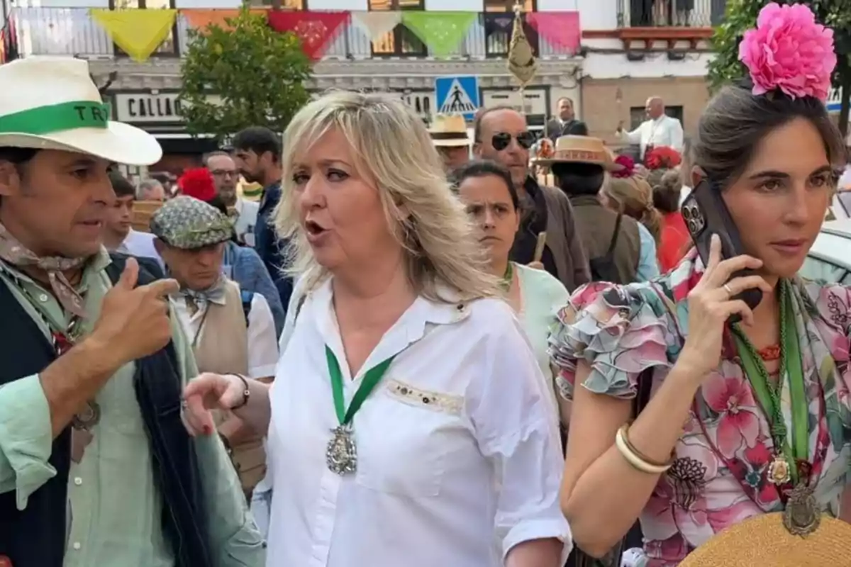 Persones vestides amb vestits típics andalusos participen en una celebració al carrer, una dona porta una flor rosa als cabells i parla per telèfon, mentre altres persones conversen i caminen entre decoracions colorides. Persones vestides amb vestits típics andalusos participen en una celebració al carrer, una dona porta una flor rosa als cabells i parla per telèfon, mentre altres persones conversen i caminen entre decoracions colorides.