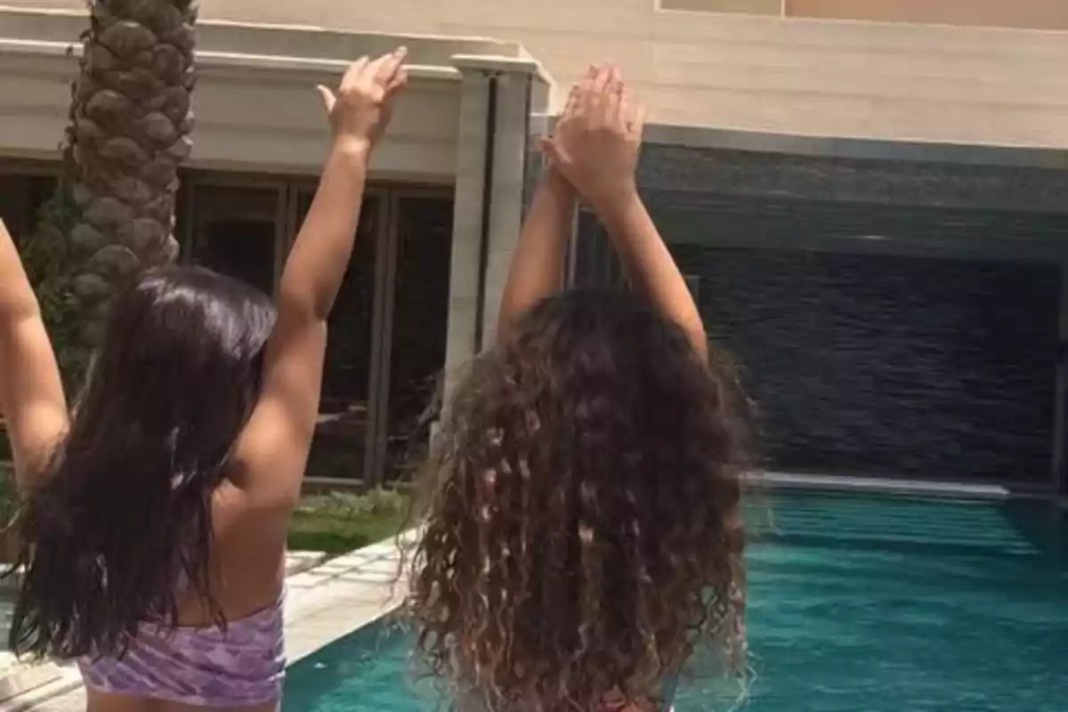 Dues nenes d'esquena aixecant els braços al costat d'una piscina. Dues nenes d'esquena aixecant els braços al costat d'una piscina.