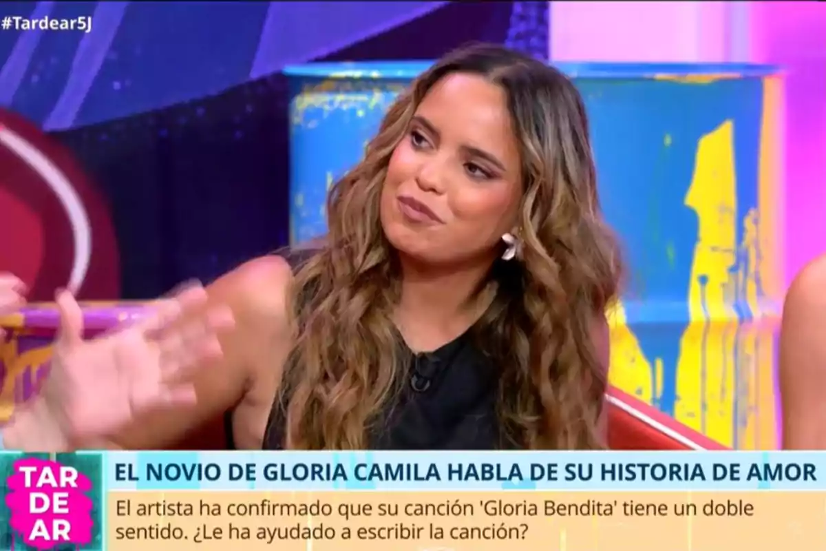 Dona amb cabell llarg i ondulat asseguda en un plató de televisió colorit durant una entrevista al programa TardeAR amb un rètol que esmenta una història d’amor i una cançó anomenada Gloria Bendita. Dona amb cabell llarg i ondulat asseguda en un plató de televisió colorit durant una entrevista al programa TardeAR amb un rètol que esmenta una història d’amor i una cançó anomenada Gloria Bendita.