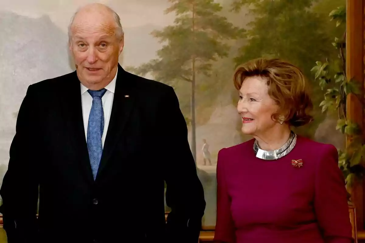 Two elegantly dressed elderly people pose in front of a painted backdrop with trees and mountains. Two elegantly dressed elderly people pose in front of a painted backdrop with trees and mountains.