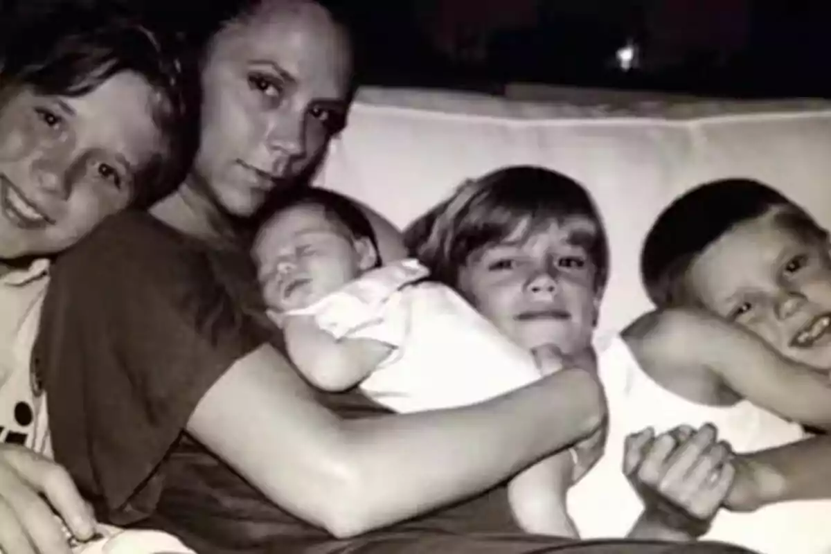 Dona asseguda en un sofà abraçant un nadó adormit i tres nens somrients al seu voltant en una foto en blanc i negre