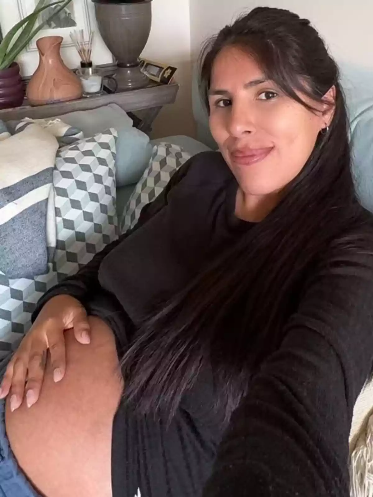 Una dona embarassada somriu mentre es fa una selfie en un sofà envoltada de coixins. Una dona embarassada somriu mentre es fa una selfie en un sofà envoltada de coixins.