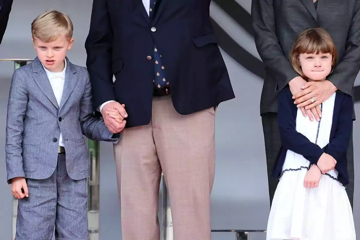 A boy and a girl are standing next to two adults, the boy is holding one of the adults' hand while the girl is being hugged by the other adult. A boy and a girl are standing next to two adults, the boy is holding one of the adults' hand while the girl is being hugged by the other adult.
