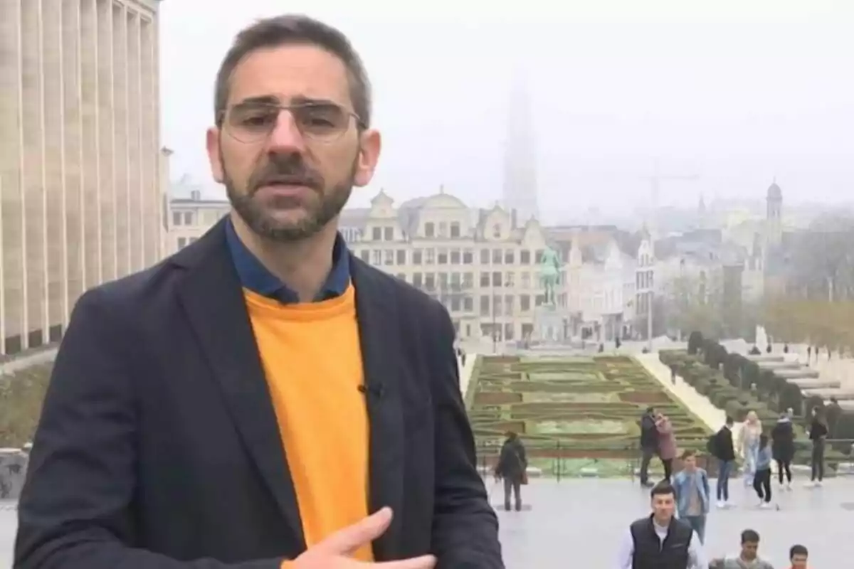 Home amb ulleres i barba en un entorn urbà amb edificis històrics i jardins al fons. Home amb ulleres i barba en un entorn urbà amb edificis històrics i jardins al fons.