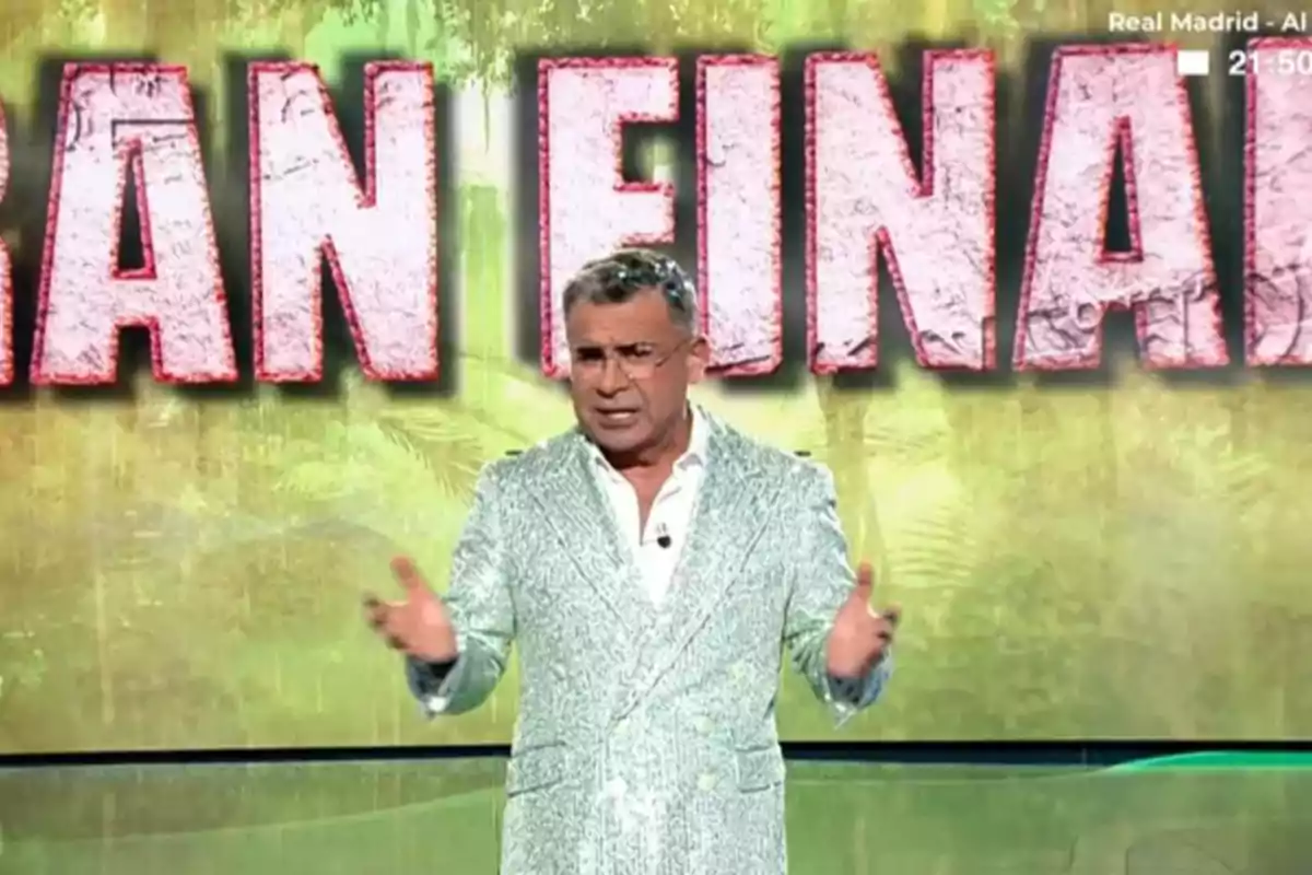 Jorge Javier Vázquez de pie con saco brillante gesticulando frente a un fondo que dice gran final Jorge Javier Vázquez de pie con saco brillante gesticulando frente a un fondo que dice gran final