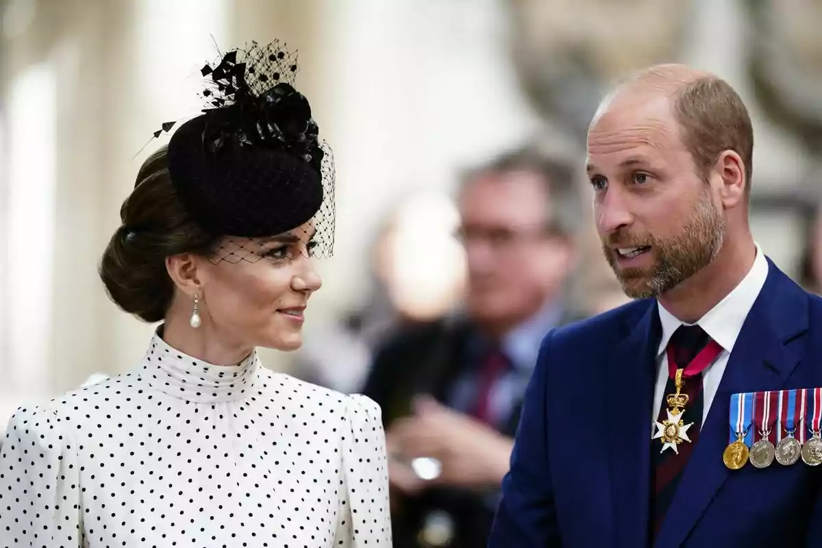 A woman in a white polka-dot dress and a black hat is talking to a man in a blue suit with medals and decorations at a formal event. A woman in a white polka-dot dress and a black hat is talking to a man in a blue suit with medals and decorations at a formal event.