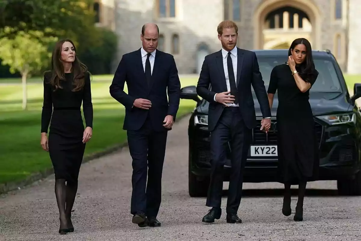 Four people dressed in black walking on a gravel path with a historic building in the background. Four people dressed in black walking on a gravel path with a historic building in the background.