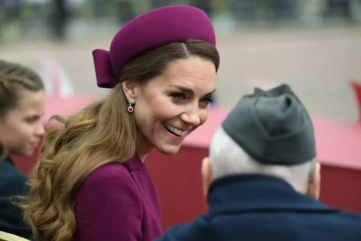 Una mujer sonriente con un sombrero morado conversa con un hombre mayor que lleva un gorro gris. Una mujer sonriente con un sombrero morado conversa con un hombre mayor que lleva un gorro gris.