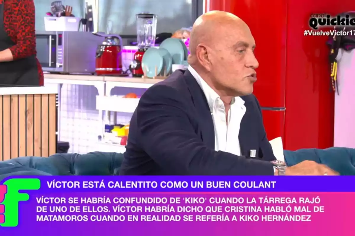 Un home calb amb vestit fosc està assegut en un plató de televisió, mentre a la pantalla apareix un text a la part inferior.