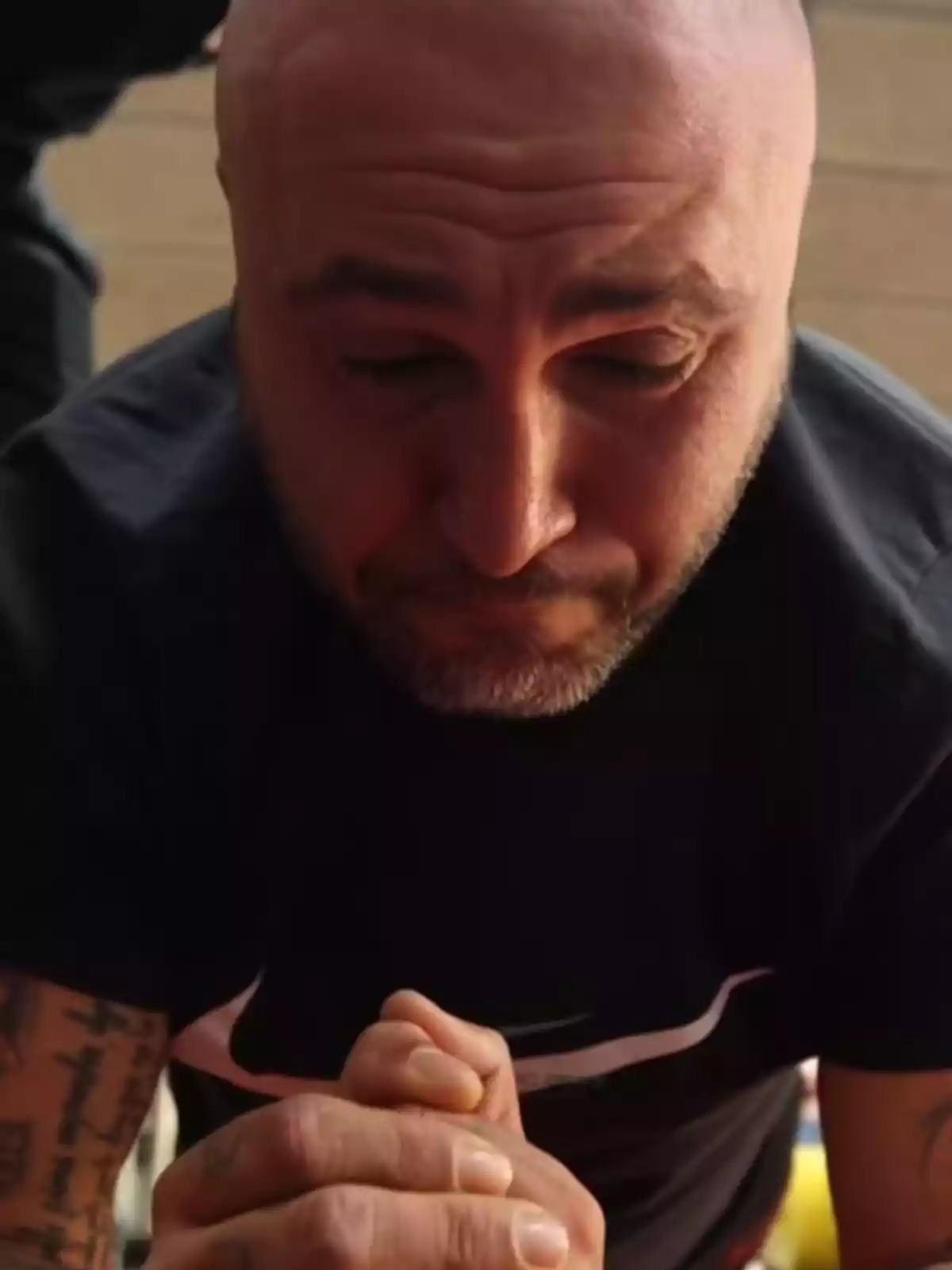 Un home calb amb barba curta i tatuatges als braços està fent una planxa, amb les mans juntes i expressió d'esforç. Un home calb amb barba curta i tatuatges als braços està fent una planxa, amb les mans juntes i expressió d'esforç.