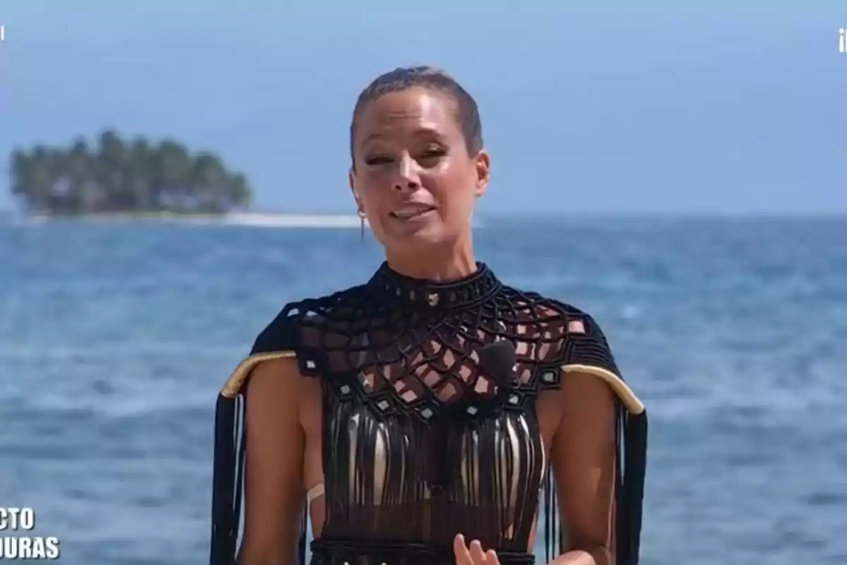 Dona dreta davant del mar amb una illa al fons i vestida amb un vestit negre amb detalls daurats Dona dreta davant del mar amb una illa al fons i vestida amb un vestit negre amb detalls daurats