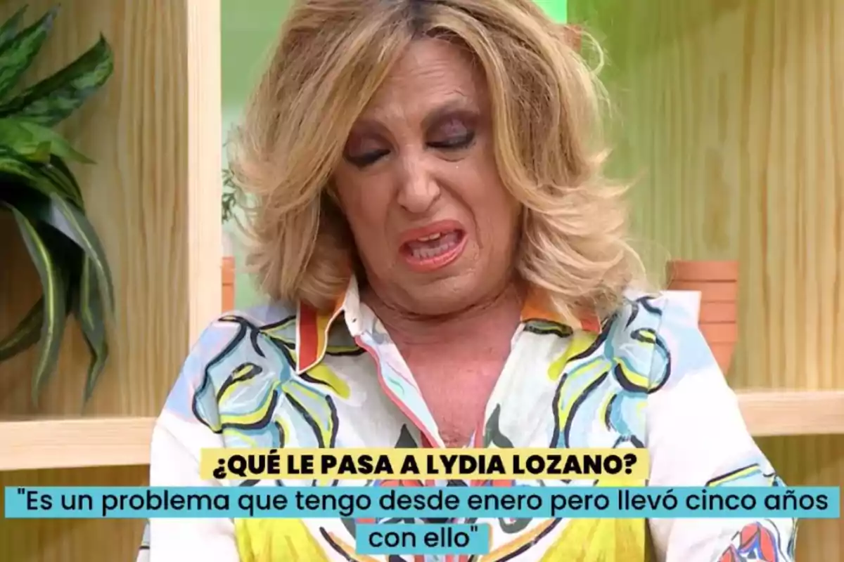 Dona rossa amb expressió de desgrat o dolor asseguda en un plató de televisió amb plantes de fons i un text a la pantalla que diu què li passa a Lydia Lozano i una cita sobre un problema de salut Dona rossa amb expressió de desgrat o dolor asseguda en un plató de televisió amb plantes de fons i un text a la pantalla que diu què li passa a Lydia Lozano i una cita sobre un problema de salut