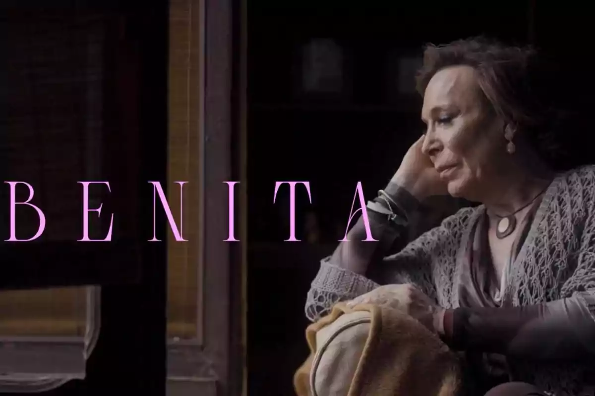 Dona gran asseguda al costat d’una finestra amb expressió pensativa i la paraula BENITA en lletres grans de color rosa Dona gran asseguda al costat d’una finestra amb expressió pensativa i la paraula BENITA en lletres grans de color rosa