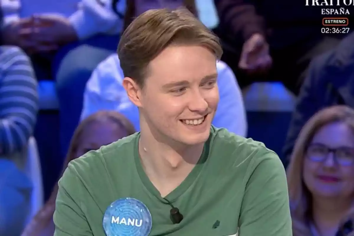 Un home jove amb samarreta verda somriu mentre està assegut en un programa de televisió, amb un públic desenfocat al fons. Un home jove amb samarreta verda somriu mentre està assegut en un programa de televisió, amb un públic desenfocat al fons.