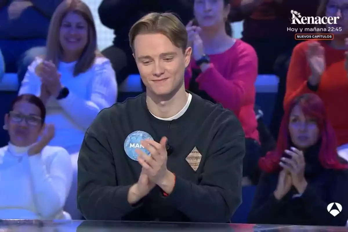 Un jove aplaudeix mentre està assegut en un programa de televisió, envoltat de persones que també aplaudeixen. Un jove aplaudeix mentre està assegut en un programa de televisió, envoltat de persones que també aplaudeixen.