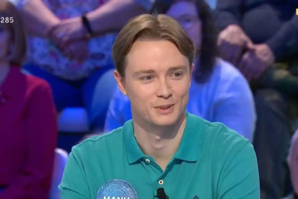Un home jove amb camisa verda somriu mentre participa en un programa de televisió amb públic al fons. Un home jove amb camisa verda somriu mentre participa en un programa de televisió amb públic al fons.