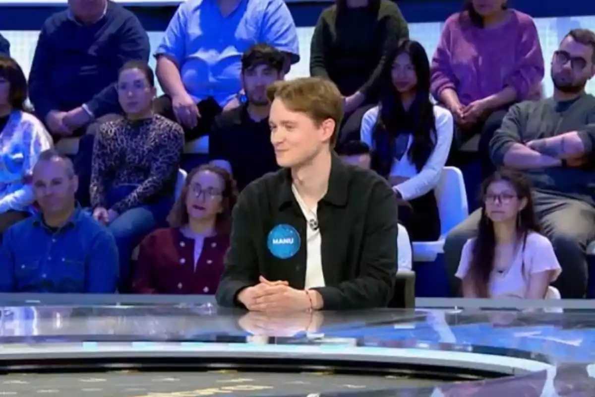 Un concursant està assegut en un plató de televisió envoltat de públic. Un concursant està assegut en un plató de televisió envoltat de públic.