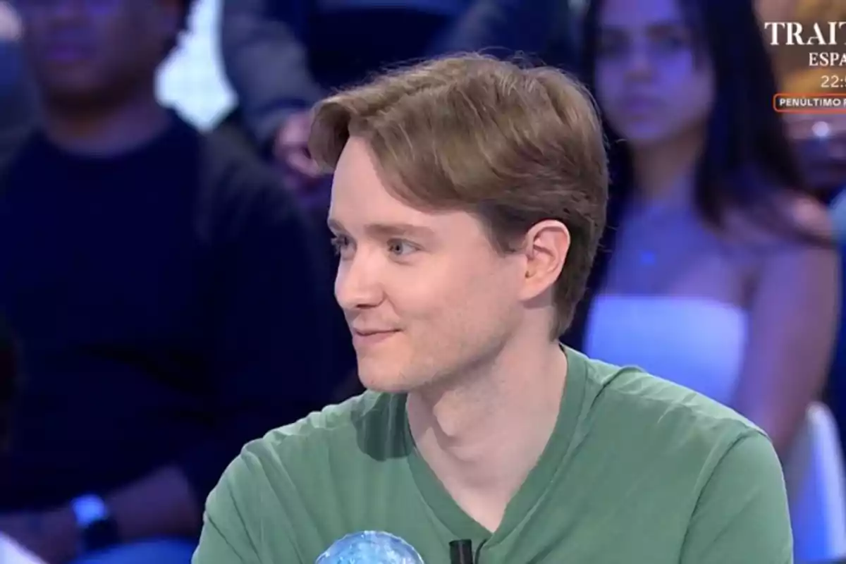 Jove de cabell castany clar i samarreta verda assegut en un estudi de televisió amb persones desenfocades al fons Jove de cabell castany clar i samarreta verda assegut en un estudi de televisió amb persones desenfocades al fons