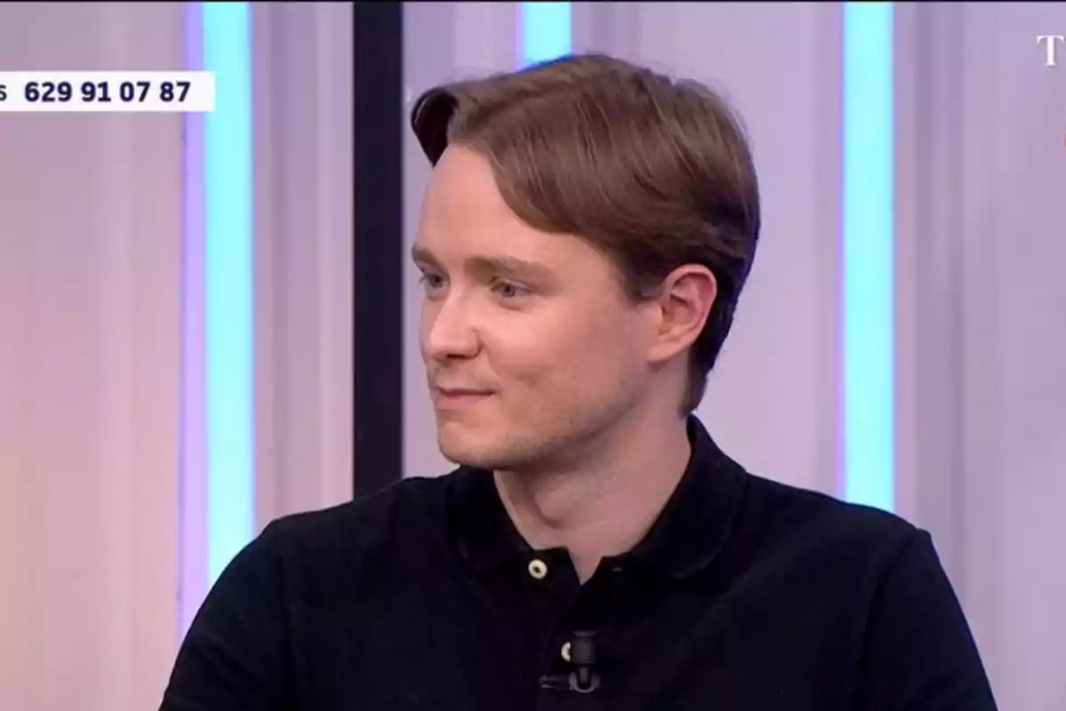 Jove de cabell castany clar i camisa negra assegut en un estudi de televisió mirant cap a la dreta Jove de cabell castany clar i camisa negra assegut en un estudi de televisió mirant cap a la dreta