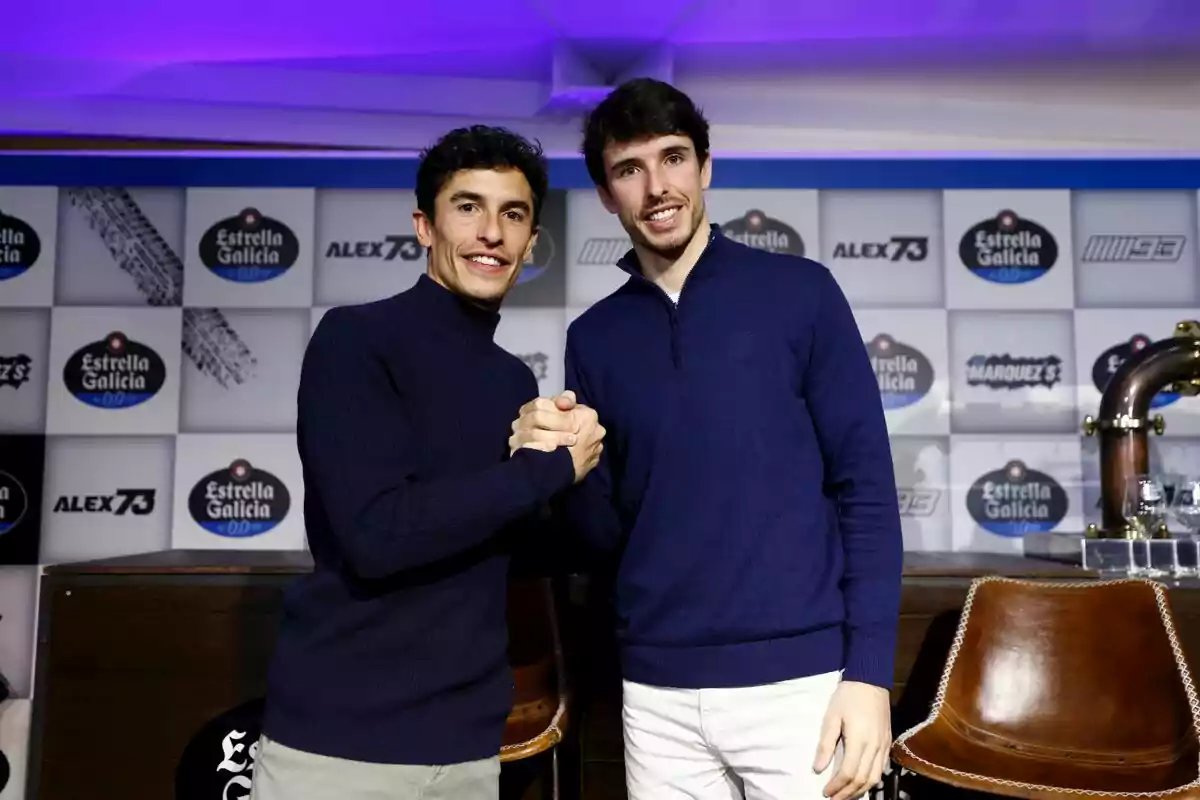 Dues persones posen juntes estrenyent-se les mans en un esdeveniment amb un fons de logotips d'Estrella Galicia. Dues persones posen juntes estrenyent-se les mans en un esdeveniment amb un fons de logotips d'Estrella Galicia.