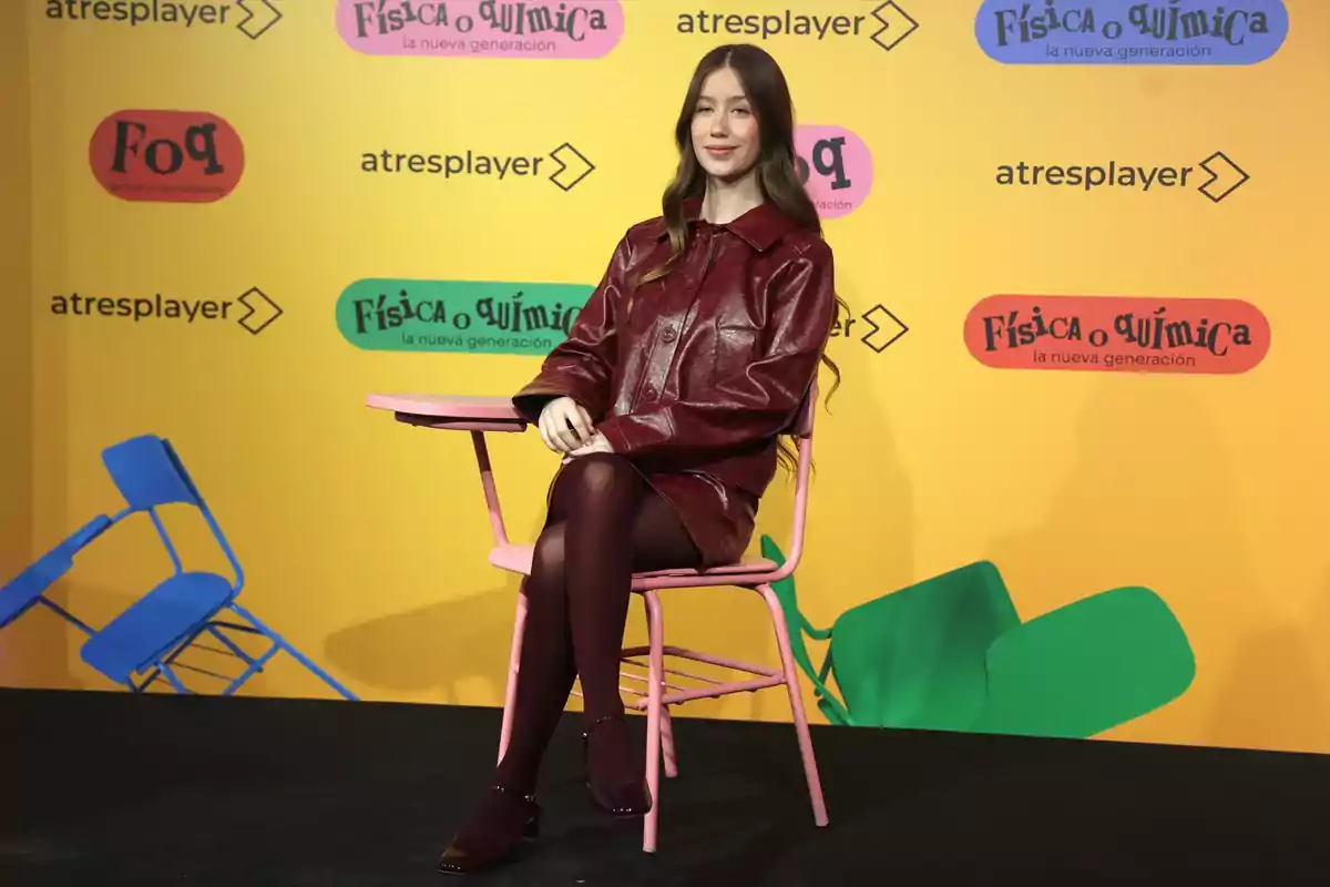 Una persona asseguda en una cadira rosa amb un fons groc que té logotips de Una persona asseguda en una cadira rosa amb un fons groc que té logotips de