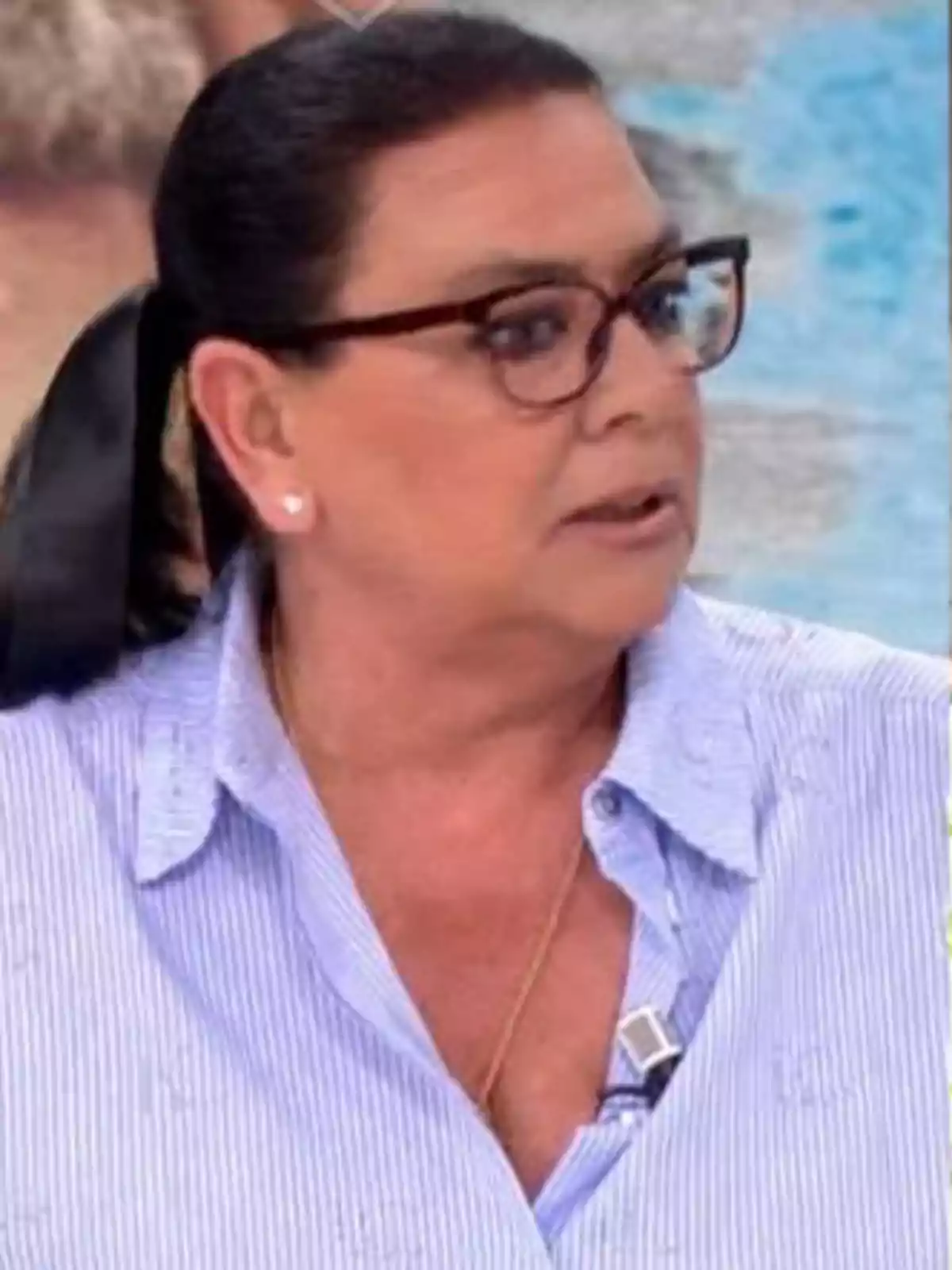 Una persona amb ulleres i cabell recollit porta una camisa de ratlles blaves i un micròfon de solapa. Una persona amb ulleres i cabell recollit porta una camisa de ratlles blaves i un micròfon de solapa.